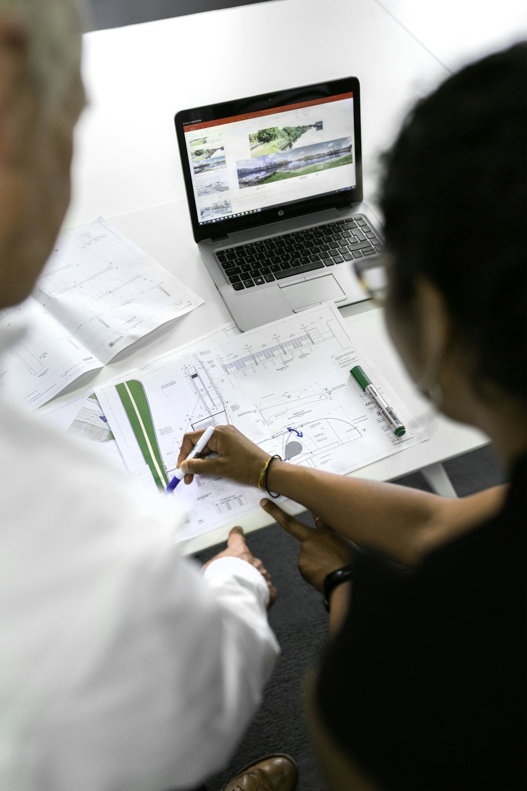 two-people-reviewing-architectural-blueprints-on-a-desk-with-a-laptop-in-a-workspace.jpg Two people reviewing architectural blueprints on a desk with a laptop in a workspace